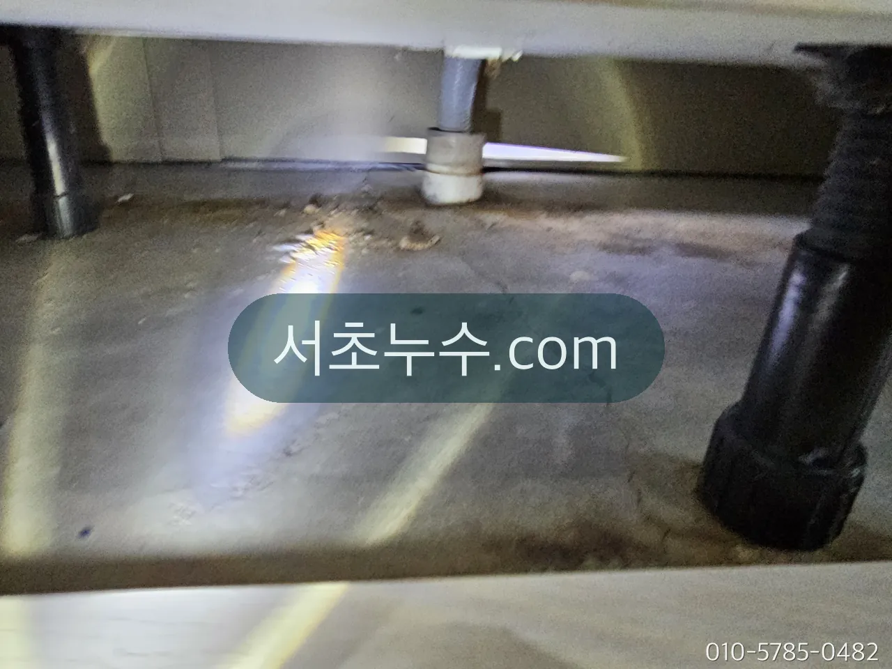 싱크대 하부장 바닥을 조명으로 점검하는 모습