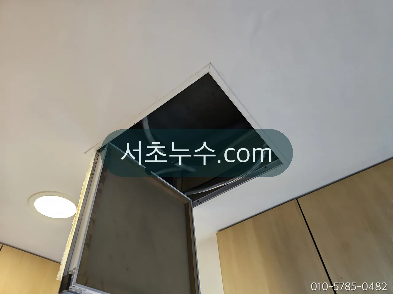 천장 점검구를 열고 안쪽 배관을 확인하는 모습