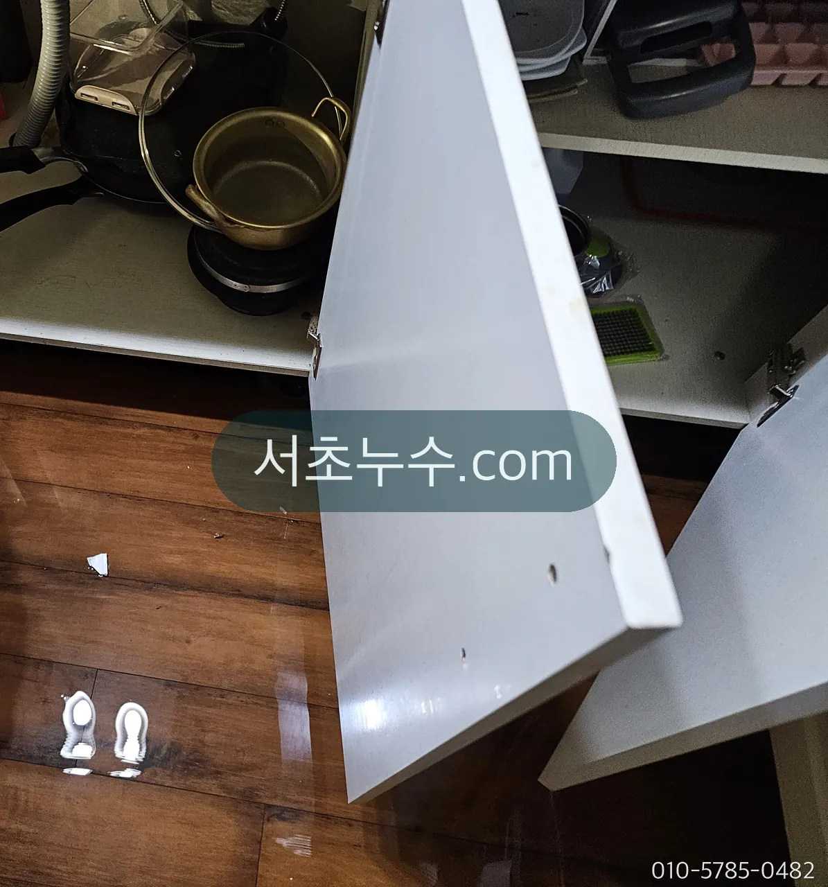 세면대 하부장 문을 떼어내고 바닥의 물기를 확인하는 장면